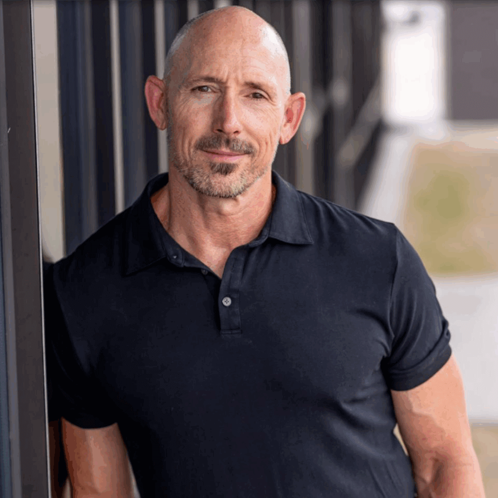 OrthoHeaven A middle-aged man with a bald head and goatee, wearing a black OrthoHeaven polo shirt, stands outdoors, leaning against a glass wall. Freedom Mapping