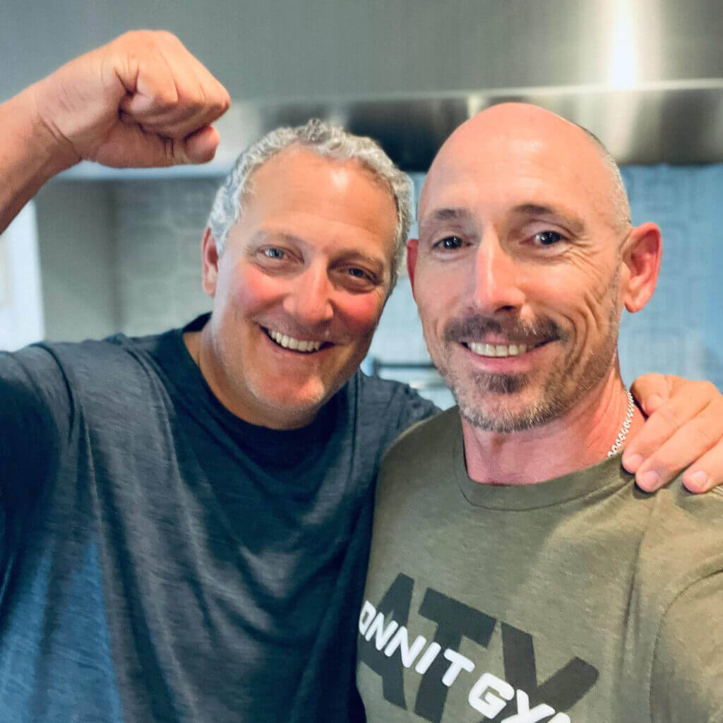 OrthoHeaven Two men stand close together indoors, smiling at the camera. One man raises his arm in a gesture of celebration, both wearing casual shirts—capturing the joyful spirit of an OrthoHeaven gathering. Freedom Mapping