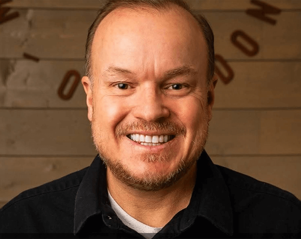 OrthoHeaven A middle-aged man with light skin, short brown hair, and a beard smiles at the camera against a wooden background, radiating the confidence of an OrthoHeaven patient. Freedom Mapping