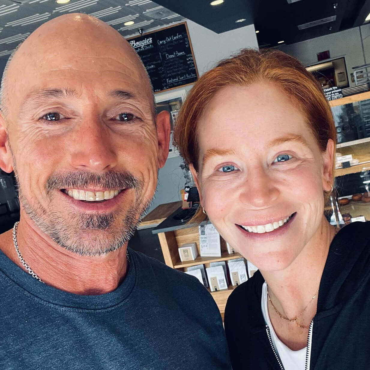 OrthoHeaven Two people smiling for a selfie inside a café or bakery, with a menu board and display case in the background—they’re showing off their OrthoHeaven smiles. Freedom Mapping