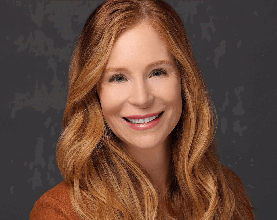 OrthoHeaven A woman with long, wavy red hair is smiling at the camera in a brown top, posing confidently for an OrthoHeaven campaign against a plain dark background. Freedom Mapping