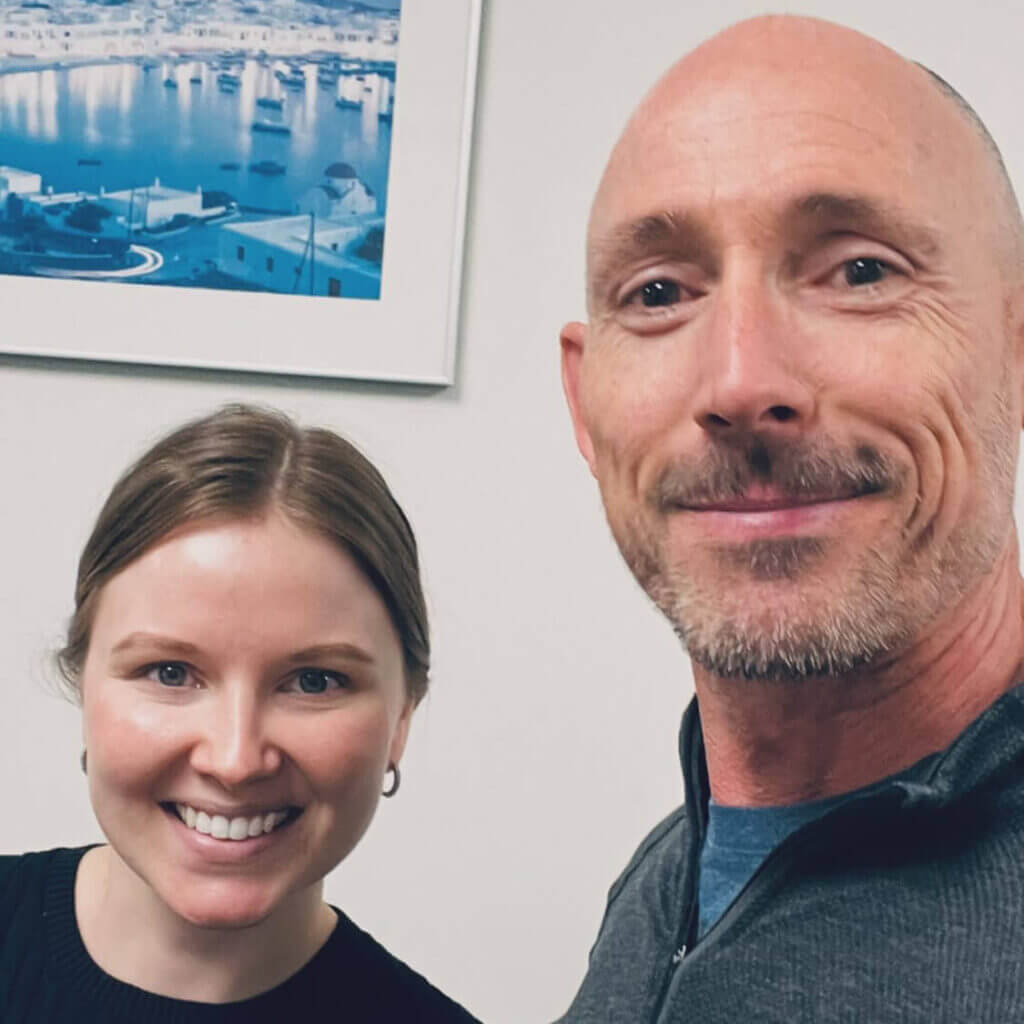 OrthoHeaven Two people smiling at the camera indoors, with a framed photo of a marina with boats hanging on the wall behind them, capture a cheerful moment at OrthoHeaven. Freedom Mapping